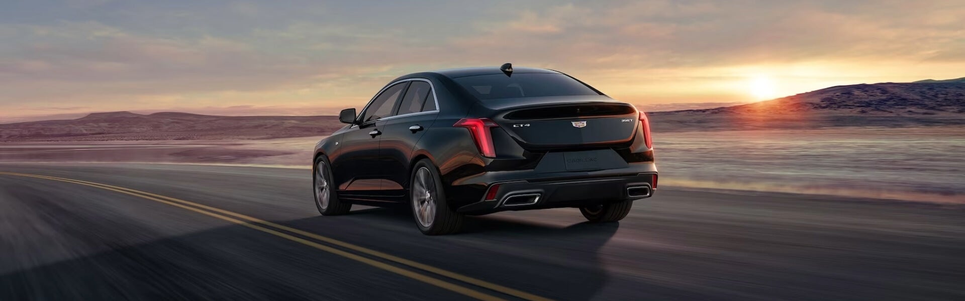 2024 Cadillac CT4 Small Luxury Sedan, Driving On A Highway With A Mountain Range and Sunset In The Background